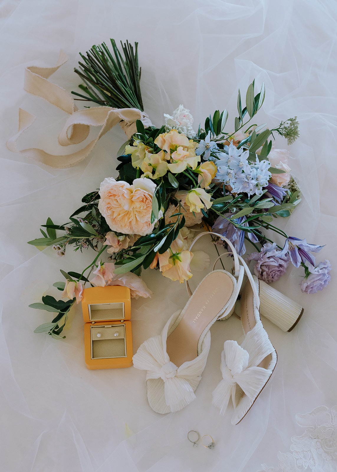 A pastel bridal bouquet with ivory shoes and pearl earrings